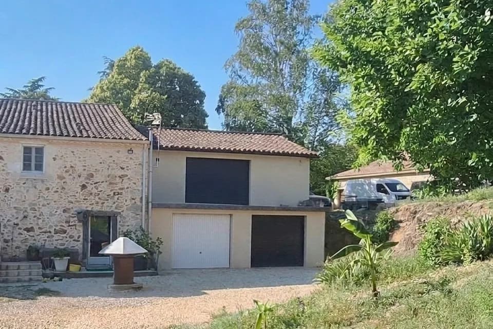 Talus enherbé devant une maison en pierre et son garage, avant travaux